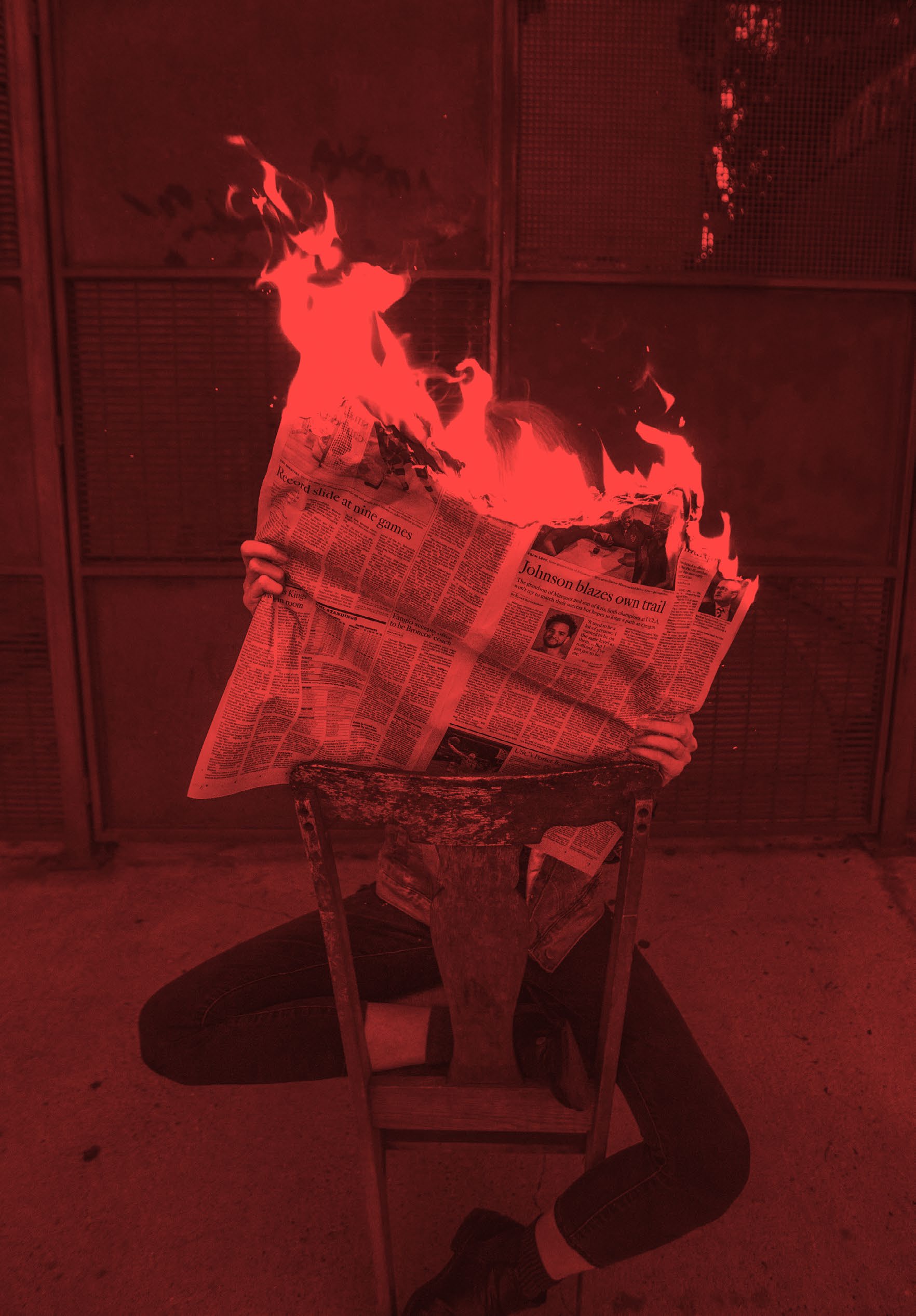 A person sitting on a chair holding a burning newspaper in front of their face.