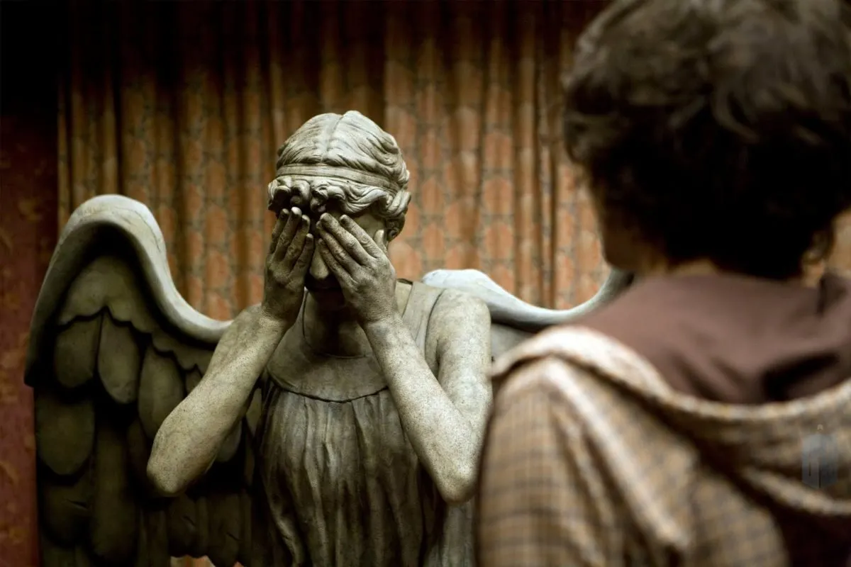 A Weeping Angel statue from Doctor Who with its hands over its face, viewed from behind the shoulder of a person.