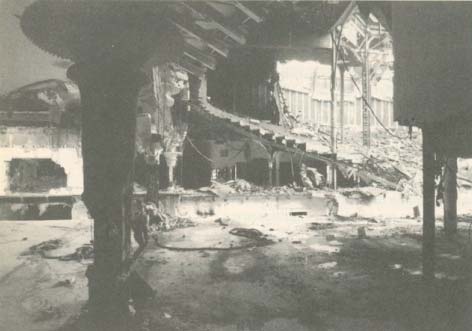 A black and white photograph of a large industrial interior, possibly a factory or power plant, with heavy machinery and structural beams.
