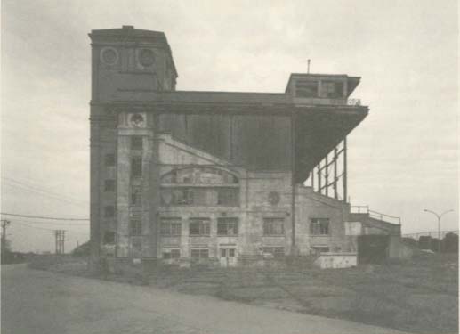 A black and white photograph of a large, industrial-style building with a prominent tower structure.