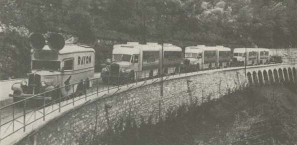 A train of vehicles, likely mobile broadcasting or surveillance units, traveling along a road.